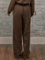 Conjunto deportivo marrón de dos piezas: campera con cremallera, cuello alto, mangas largas con puño y detalles de rayas blancas en mangas y laterales del pantalón. Pantalón recto de cintura alta con cordón ajustable.