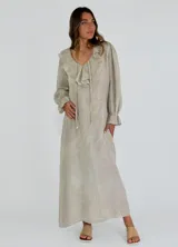 Vestido largo color beige de lino, con escote en V con volados y lazo ajustable, mangas largas con puños elásticos y bolsillos laterales.