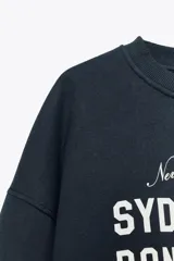 Sudadera azul marino de cuello redondo y manga larga con estampado frontal que dice "New South Wales Sydney 1985 Bondi Beach" en color blanco.