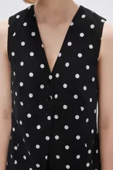 Chaleco largo sin mangas negro con estampado de lunares blancos, cuello en V y corte entallado.