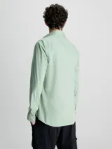 Camisa verde claro de popelín elástico, corte slim, con cierre frontal de botones, mangas largas y logo de Calvin Klein bordado en el pecho.