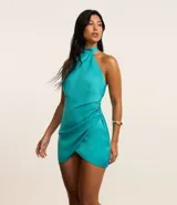 Vestido corto de satén color turquesa, con escote halter y lazo en el cuello. Presenta un drapeado lateral y falda cruzada.