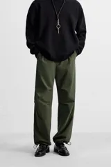 Pantalón verde militar de corte relaxed fit confeccionado en tejido técnico ligero. Cuenta con cintura elástica ajustable con cordón interior, bolsillos frontales y traseros con solapa, pliegues en las rodillas y bajo ajustable con elástico.