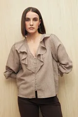 Camisa a rayas color beige con finas líneas verticales negras, de manga 3/4 con puños elastizados, escote en V con volados y cierre frontal con botones de nácar.