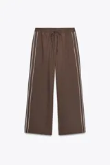 Pantalón marrón de tiro alto con cintura elástica ajustable con cordones, corte ancho y bolsillos laterales. Presenta una banda lateral blanca con diseño de eslabones.