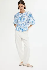 Blusa blanca con estampado floral azul, cuello redondo, cierre de botones y mangas globo tres cuartos con puños elásticos.