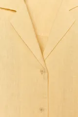 Camisa de lino color amarillo claro, de corte recto, con cuello solapa, escote en pico, cierre frontal con botones y mangas largas con puños abotonados.