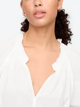 Blusa blanca de manga corta con escote en V y detalle de volados en el cuello.