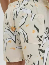 Short de baño color crema con estampado de flores y hojas en blanco, negro y amarillo. Tiene cintura elástica con cordón ajustable, bolsillos laterales y un bolsillo trasero.