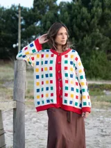 Cárdigan de punto color crudo con botones y ribete rojo. Presenta un patrón de cuadrados de colores (azul, rojo, amarillo y verde).
