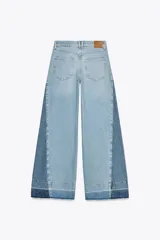 Pantalón de jean de tiro medio con cinco bolsillos, corte wide leg y detalle de tejido con lavado lateral combinado. Cierre frontal con cremallera y botón.