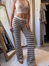 Conjunto de dos piezas tejido a crochet, compuesto por un top halter y un pantalón acampanado. El tejido es calado con rayas horizontales en tonos beige claro y marrón.