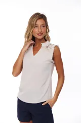 Blusa color crema con escote en V, sin mangas y detalle de encaje en hombros y cuello.
