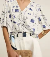 Blusa de mangas abullonadas cortas, confeccionada en Viscolino con 15% de Lino, con cuello v con lazo y estampa de accesorios de playa.