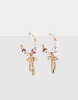 Aros tipo argolla dorados con cuentas de perlas, dijes de cerámica con estampado floral y dije de moño metálico.