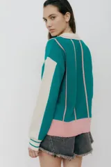 Buzo tipo polo de punto con rayas verticales en tonos beige, marrón y rosa. Tiene cuello polo marrón, cierre parcial con botones amarillos y terminaciones acanaladas en puños y ruedo.