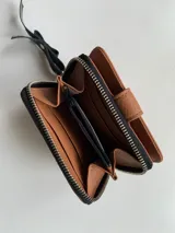 Billetera de cuero color plateado con cierre metálico, cuenta con múltiples compartimentos para tarjetas, billetes y monedas.