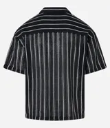 Camisa masculina modelo boxy, confeccionada en punto, con cuello polo, manga corta, cierre por botones y estampa de rayas verticales blancas sobre fondo negro.