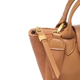 Cartera de mano y hombro color habano, con cuerpo de tela tejida y detalles en cuero sintético liso. Presenta un bolsillo frontal con solapa y broche dorado, asas cortas y correa larga regulable y desmontable. El logo 'XL' está aplicado en el centro del bolsillo frontal.