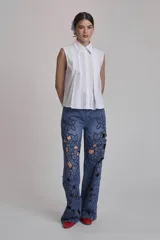 Camisa blanca sin mangas con cuello clásico, cierre frontal con botones y detalle de plisado vertical en el frente.