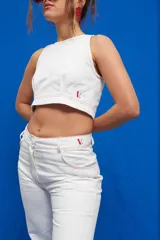 Pantalón de gabardina color blanco, de corte recto y tiro medio/alto, con bolsillos delanteros y traseros al estilo jean. Los pespuntes en contraste son de color rojo.