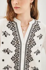 Camisa blanca de manga larga con cuello mao y escote en V. Presenta bordados florales en blanco y dorado en el frente.