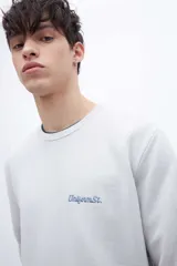 Buzo celeste de felpa liviana con cuello redondo, puños en mangas y bajo holgado. Tiene un bordado pequeño en el pecho con la inscripción "Uniform St.".