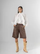 Camisa blanca de algodón italiano con cuello alto ajustable mediante lazo trasero, mangas abullonadas y un gran shabot frontal con volados en cascada.