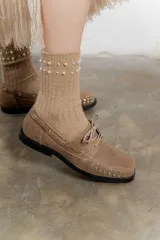 Mocasín de cuero color marrón con tachas metálicas plateadas en la puntera y laterales.