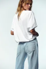 Camiseta blanca de algodón con cuello redondo, mangas cortas y bajo asimétrico ajustable con lazadas.