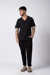 Camisa tejida color crudo, de manga corta, con cuello bowling y botones frontales. Presenta un tejido con textura de trenzas verticales y rib negro en los puños.