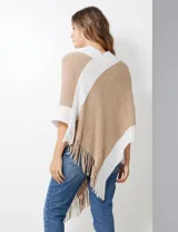 Poncho de tejido soft, color beige y blanco, con diseño cruzado en el frente y cuello en V. Presenta bordes y flecos en color blanco.