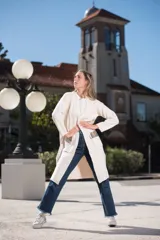 Saco largo color crudo, con cuello redondo, bolsillos frontales con apliques de cuero plateado y mangas largas.