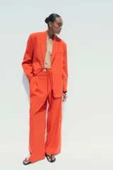 Pantalón de vestir color naranja, de tiro alto y pernera ancha. Presenta doble pliegue frontal, trabillas en la cintura, bolsillos laterales y falsos bolsillos de vivo en la espalda.
