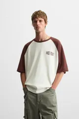 Camiseta blanca con mangas cortas marrones tipo ranglán, cuello redondo y estampado con la frase "Inner Peace" en marrón.