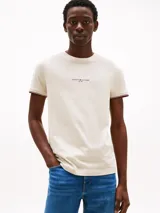 Remera Tommy Hilfiger color crema de corte slim fit, cuello redondo y mangas cortas con ribete distintivo en rojo, blanco y azul. Logo de la marca bordado en el pecho.