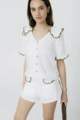 Blusa blanca de lino con cuello y mangas cortas con volados con borde de crochet marrón.