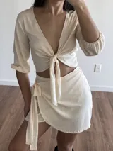 Conjunto color crudo compuesto por un top corto con escote en V y mangas 3/4 abullonadas, con cierre frontal anudado, y una minifalda cruzada con lazo lateral.