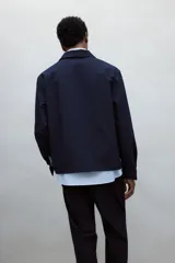 Sobrecamisa azul marino de corte recto, con cuello inglés, cierre frontal con botones, mangas largas con puños abotonados, dos bolsillos de parche en el pecho y canesú en la espalda.