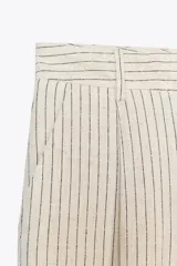 Pantalón de tiro alto color crudo con finas rayas verticales negras, pinzas delanteras, bolsillos frontales y falsos bolsillos de vivo en la espalda.