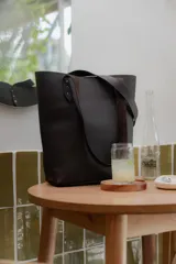 Bolso tipo tote de cuero color marrón oscuro, con doble asa de hombro y broche central.