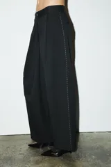 Pantalón negro de tiro medio con trabillas, falso bolsillo de vivo en espalda, detalle de pespuntes combinados a contraste y pinzas. Cierre frontal con cremallera y botón.