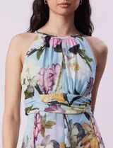 Vestido largo de gasa estampada con flores en tonos celeste, rosa y verde. Tiene cuello halter con abertura en forma de ojal, corte en la cintura con faja plisada y abertura central en la espalda con cierre invisible.