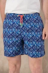 Short de baño azul vibrante con estampado repetitivo de cruces pequeñas en blanco y rojo. Presenta cintura elástica fruncida y cordón de ajuste trenzado en color coral con puntas de neón verde lima.