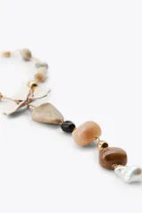 Collar con cadena dorada de eslabones y cuentas de resina en tonos beige y blanco. Dije central con forma de flor esmaltada y colgante con piedras de diferentes tamaños y colores.