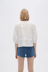 Blusa blanca de algodón con textura de lunares, corte recto, cuello redondo, mangas 3/4 abullonadas y cierre frontal con botones.