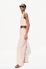Pantalón de vestir color rosa pálido, de tiro alto, con pinzas delanteras, bolsillos laterales, pierna ancha y cierre frontal con cremallera y botón.