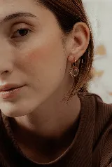 Par de aros colgantes con argollas doradas y dijes circulares de resina transparente con incrustaciones de strass de colores. El dije mide aproximadamente 1.5cm de diámetro.