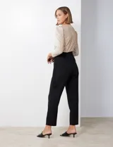 Enterito de fiesta con torso de lentejuelas color champagne, escote en V cruzado, mangas 3/4 con frunces en los hombros, cintura elastizada con lazo negro y pantalón negro de corte recto con bolsillos laterales.
