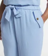 Pantalón de crepé celeste, modelo zanahoria, con elástico y lazo en la cintura. Presenta bolsillos traseros simples y bolsillos delanteros con solapas y botones metalizados.